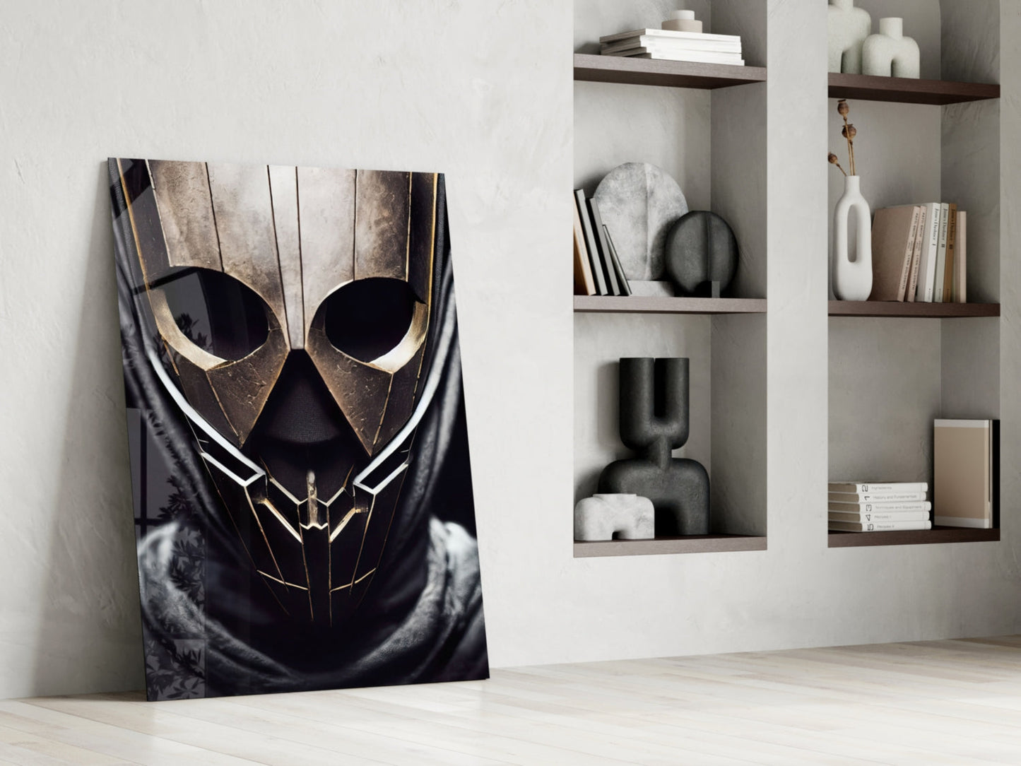 Dark glass art panel with gold-trimmed skull design leaning against white wall beside shelving unit with books and decorative objects.