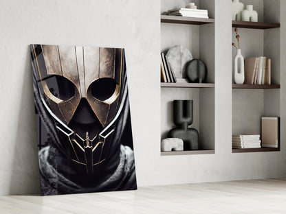 Dark glass art panel with gold-trimmed skull design leaning against white wall beside shelving unit with books and decorative objects.