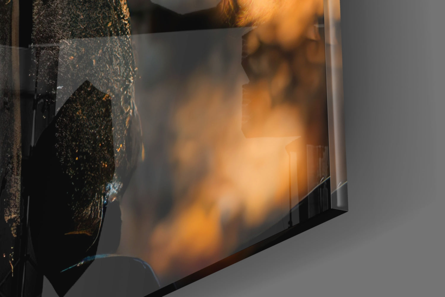 Close-up side view of glass art piece with black textured surface and golden-orange flame-like patterns casting warm shadows.