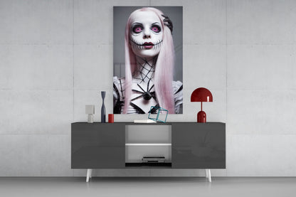 Glass wall art featuring pale-skinned figure with pink hair, stitched mouth, and pink eyes displayed above gray console table with red lamp and decorative objects.