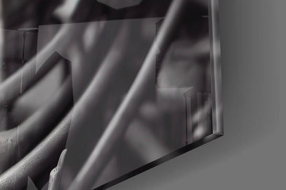 Close-up detail of clear glass art piece showing layered cylindrical forms with soft shadows and light reflections on gray surface.