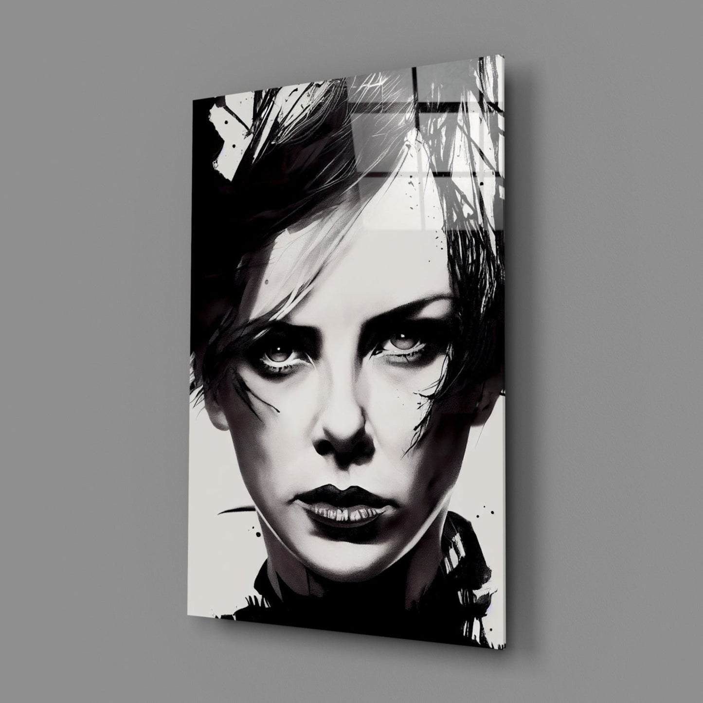 Black and white portrait on glass wall art mounted at an angle against gray background, showing close-up of face with dramatic eye makeup and short dark hair.