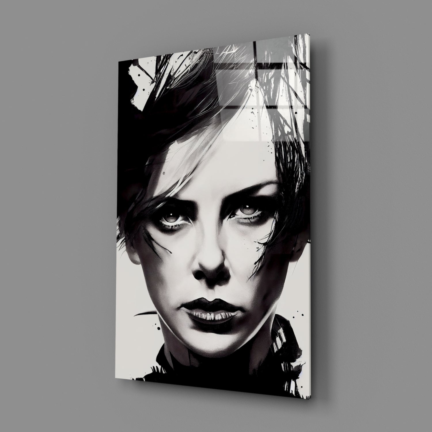 Black and white portrait on glass wall art mounted at an angle against gray background, showing close-up of face with dramatic eye makeup and short dark hair.