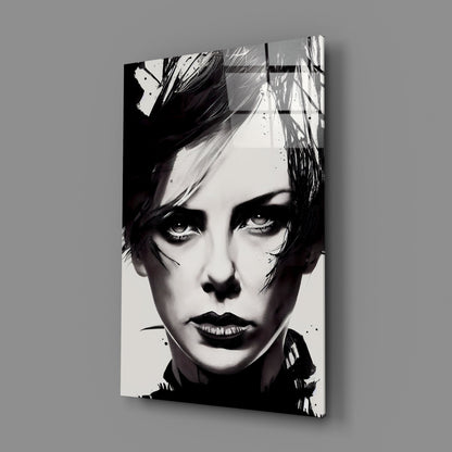 Black and white portrait on glass wall art mounted at an angle against gray background, showing close-up of face with dramatic eye makeup and short dark hair.