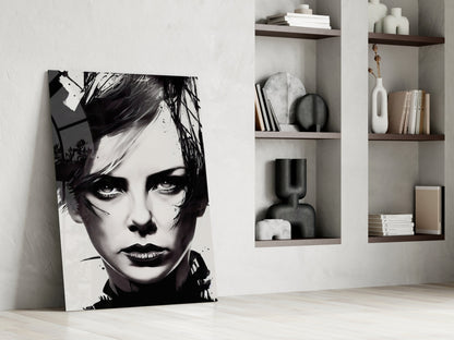 Black and white portrait glass wall art leaning against white wall beside wooden floating shelves with books and decorative objects.
