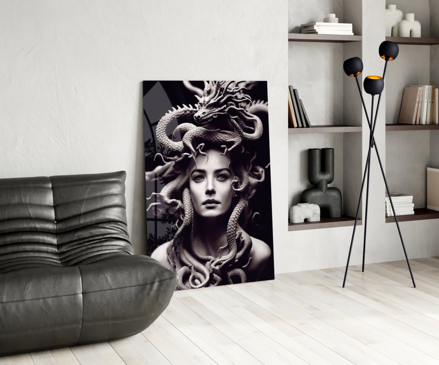Monochromatic Medusa glass art leaning against white wall in modern living room with gray leather sofa and shelving.