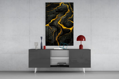 Black and gold abstract lava-pattern glass art displayed above gray media console in modern living room setting.