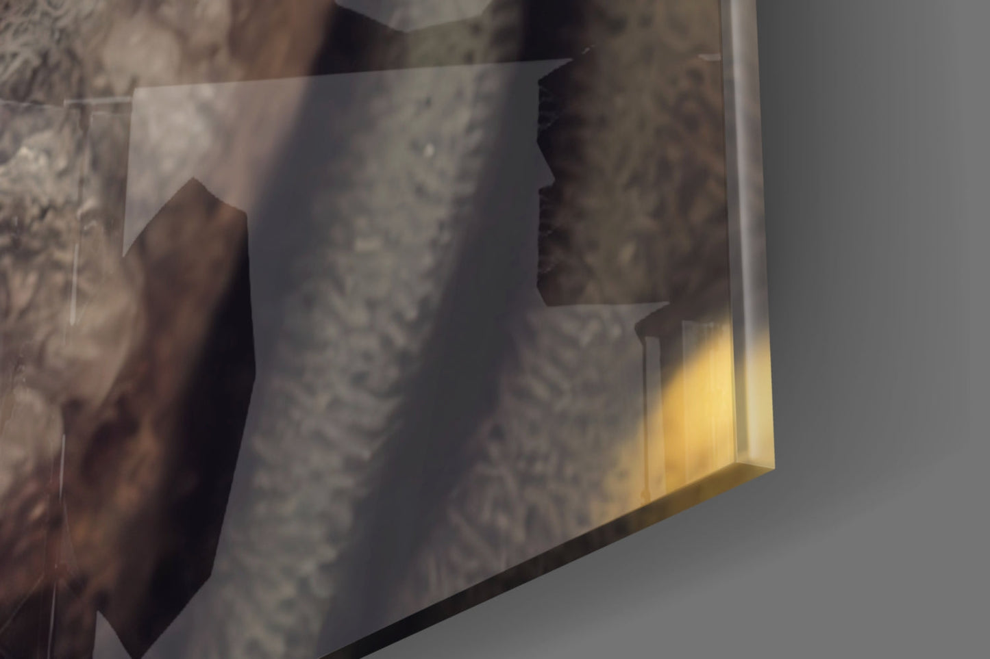 Close-up angled view of translucent glass art with brown organic shapes and yellow-tinted interior against gray background.