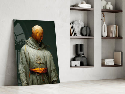 Glass art print leaning against white wall shows robed figure with golden sphere head and orange sash against dark green background.