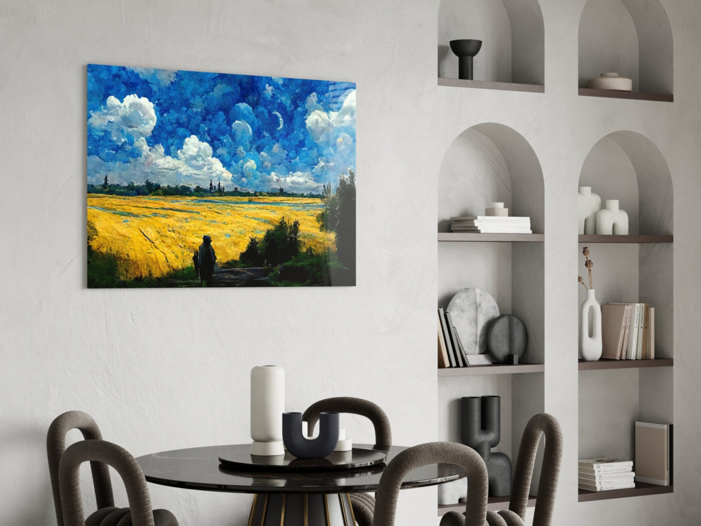 Glass art print depicting a golden wheat field with blue sky and white clouds, displayed above a black dining table in a modern interior.
