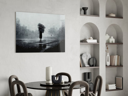 Black and white glass art depicting a solitary figure with umbrella in rainy landscape, displayed above dining table in minimalist interior.