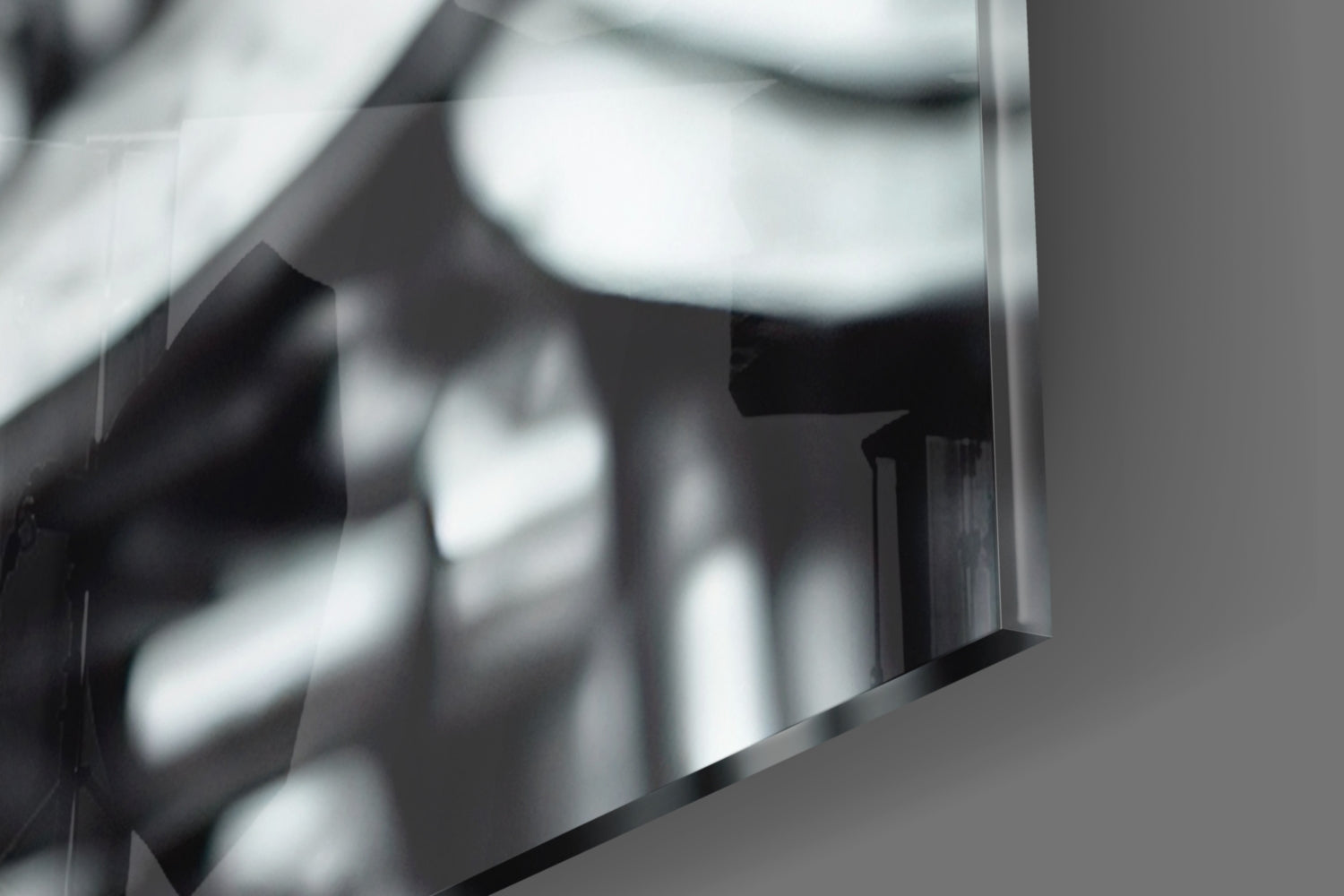 Close-up detail of polished black glass art piece showing reflective surface and beveled edge against neutral background.