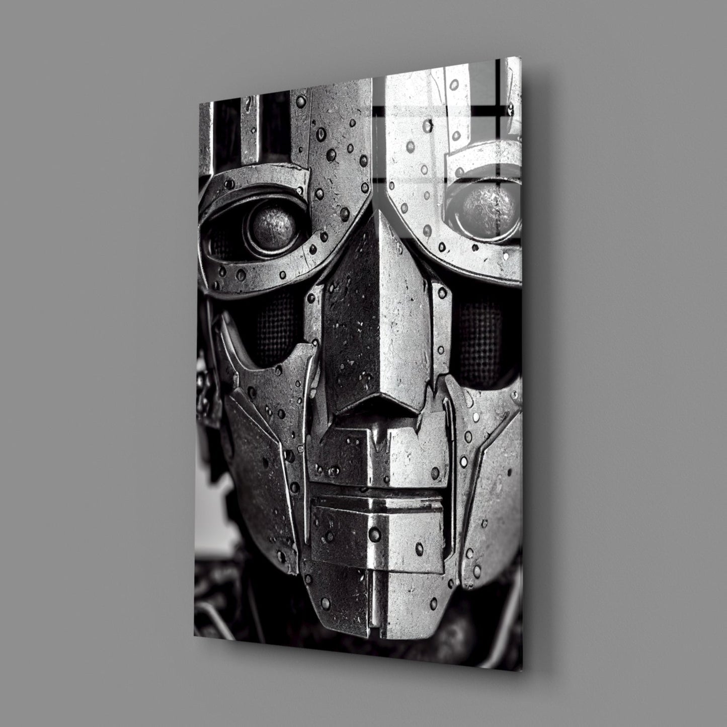 Black and white photograph of a metallic robotic head with riveted armor plating and circular eye openings, displayed at an angle against gray background.