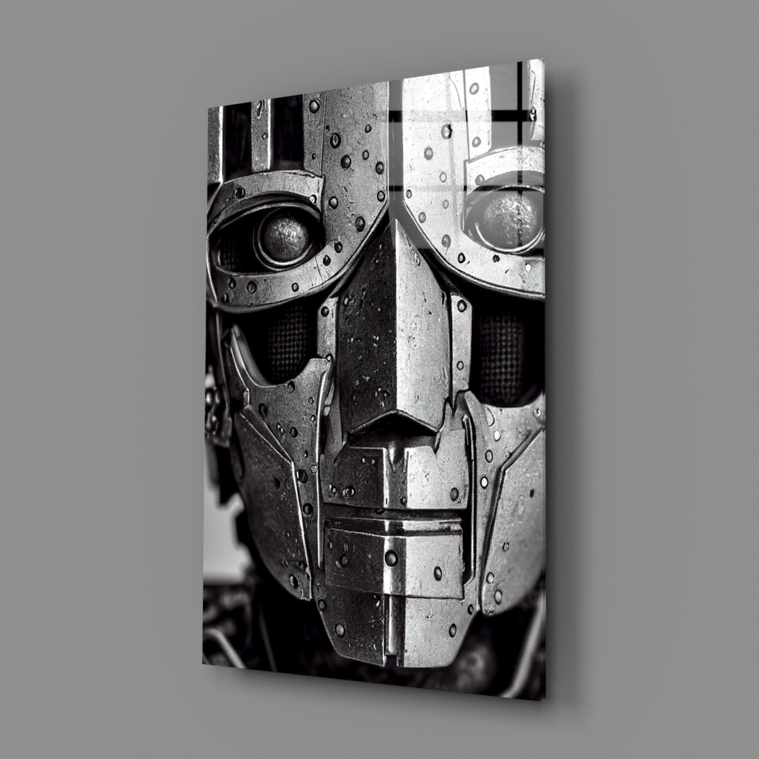 Black and white photograph of a metallic robotic head with riveted armor plating and circular eye openings, displayed at an angle against gray background.