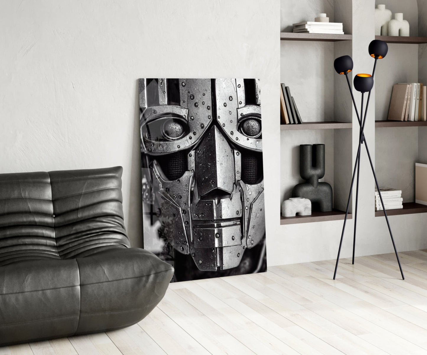 Modern living room interior featuring a black leather curved sofa, monochromatic robotic face canvas artwork, tall black floor lamp with spherical gold-lined shades, and wooden wall shelving with books and décor.