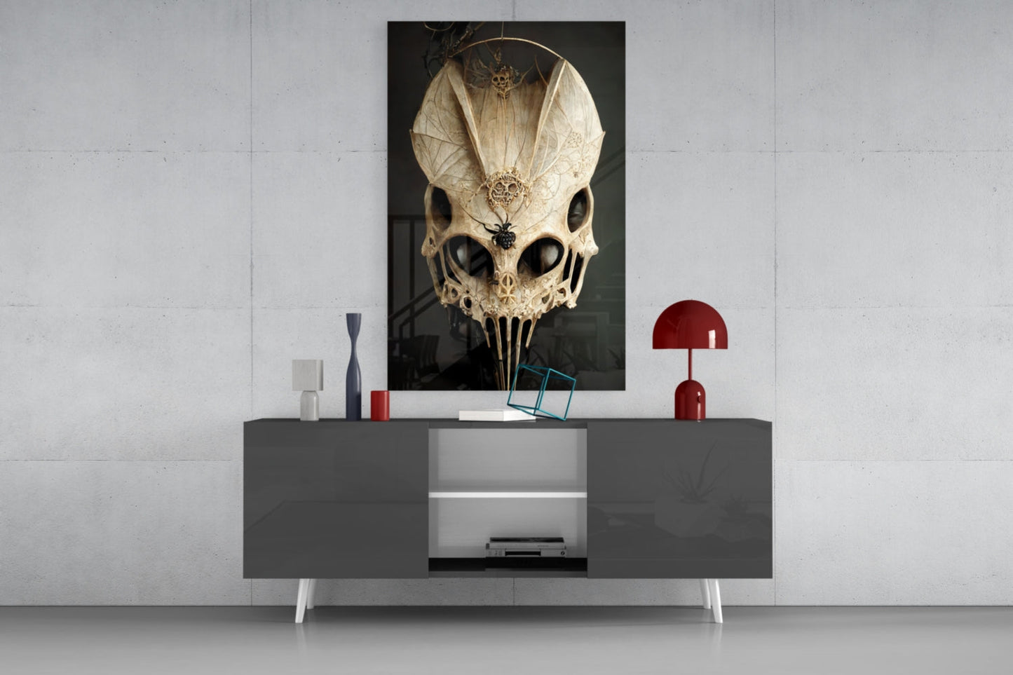 Ornate cream and black skull glass art displayed on dark gray sideboard with red lamp and decorative objects against white wall.