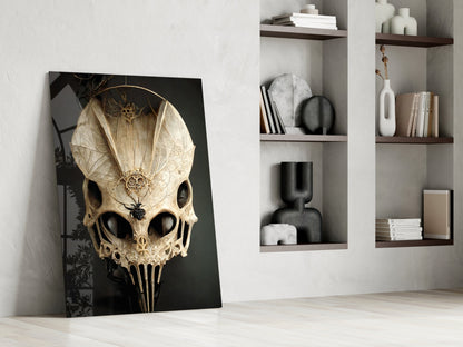 Ornate cream and gold skull glass art leaning against white wall beside shelving unit displaying decorative objects.