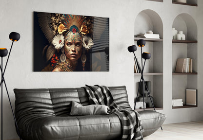Glass wall art depicting an ornately decorated woman with feathered headdress and golden facial markings displayed above a gray leather sofa in a modern living room interior.