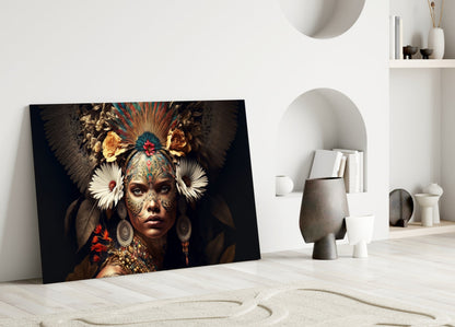 Glass art print leaning against white wall showing ornately decorated woman's face with feathered headdress and gold, red, and teal embellishments.