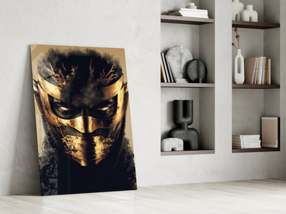 Leaning against white wall, gold and black masked face glass art panel beside white shelving unit with decorative objects and books.