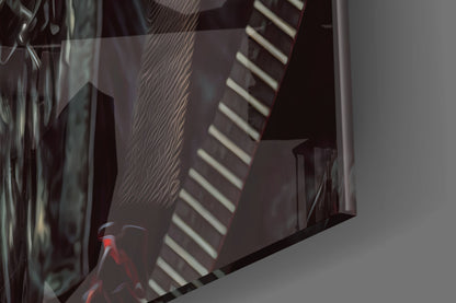 Close-up angled view of glass wall art with dark geometric shapes, striped patterns, and red accents cast against light background.