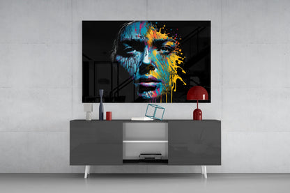Colorful splash glass wall art featuring a portrait with blue and yellow paint effects displayed above a gray media console in a modern interior setting.