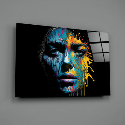 Angled view of glass wall art featuring a colorful portrait with blue, yellow, and magenta paint splashes on black background.