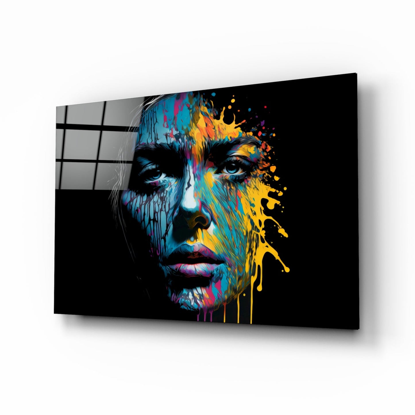 Angled perspective of a glass wall art panel displaying a colorful splatter portrait with vibrant blue, yellow, and pink paint effects on black background.