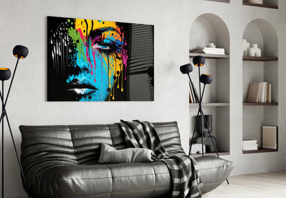 Colorful pop art portrait with vibrant yellow, blue, and pink paint drips displayed above a gray leather sofa in modern living room setting.