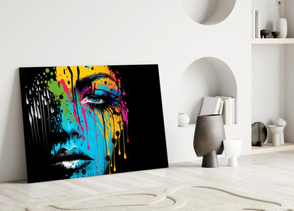 Colorful pop art glass wall panel with multicolored paint splatter design on black background, leaning against white wall in minimalist room setting.