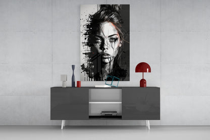 Black and white portrait glass art with ink splatter effects displayed above gray console table with red lamp and decorative objects.