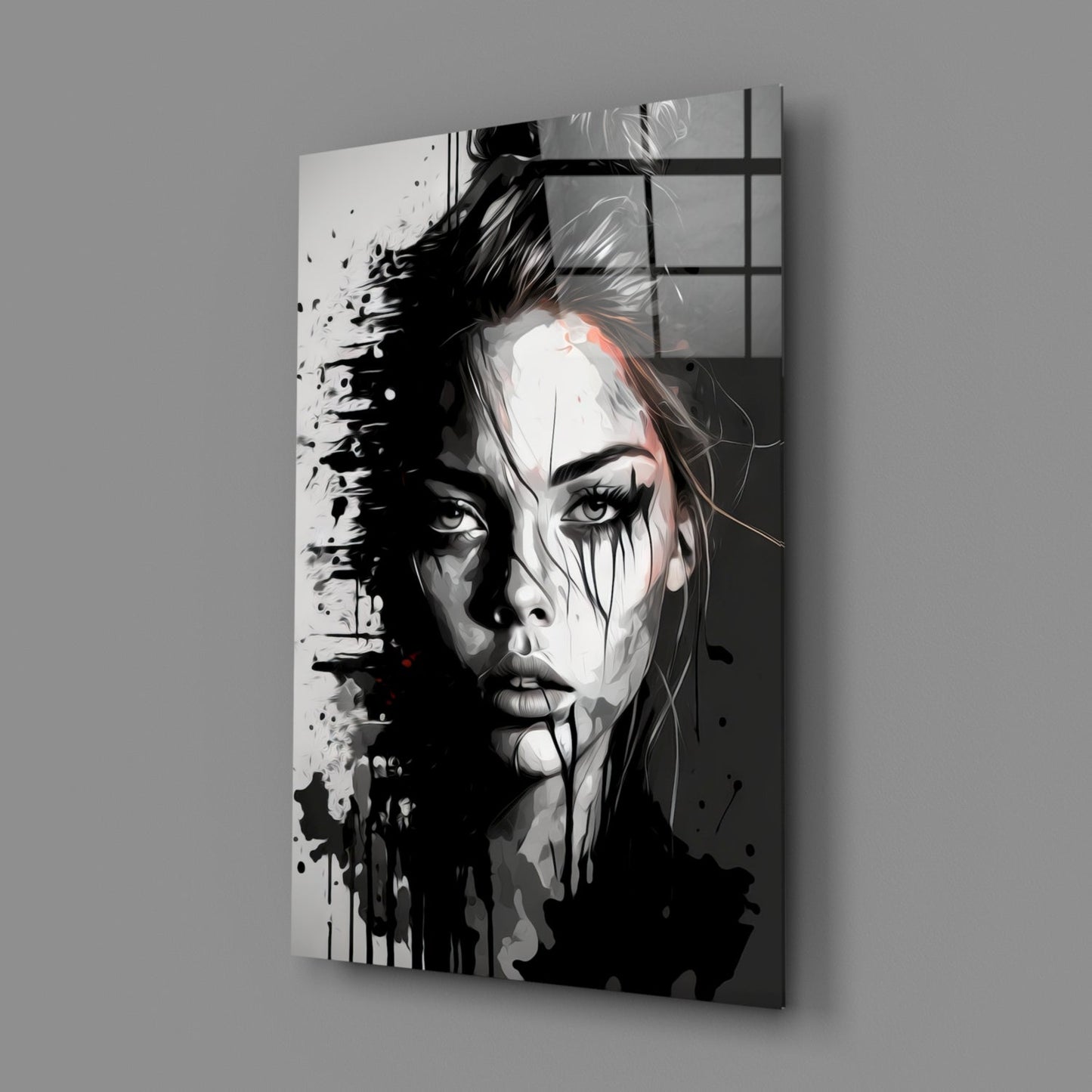 Angled view of a black and white portrait glass wall art panel with splatter effects and a woman's face against a gray wall.