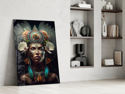 Glass wall art leaning against white wall displays portrait of woman with ornate floral headdress and facial tattoos in dark tones.