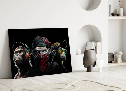 Neon lines glass wall art leaning against white wall displays three stylized monkeys with colorful accents on black background.