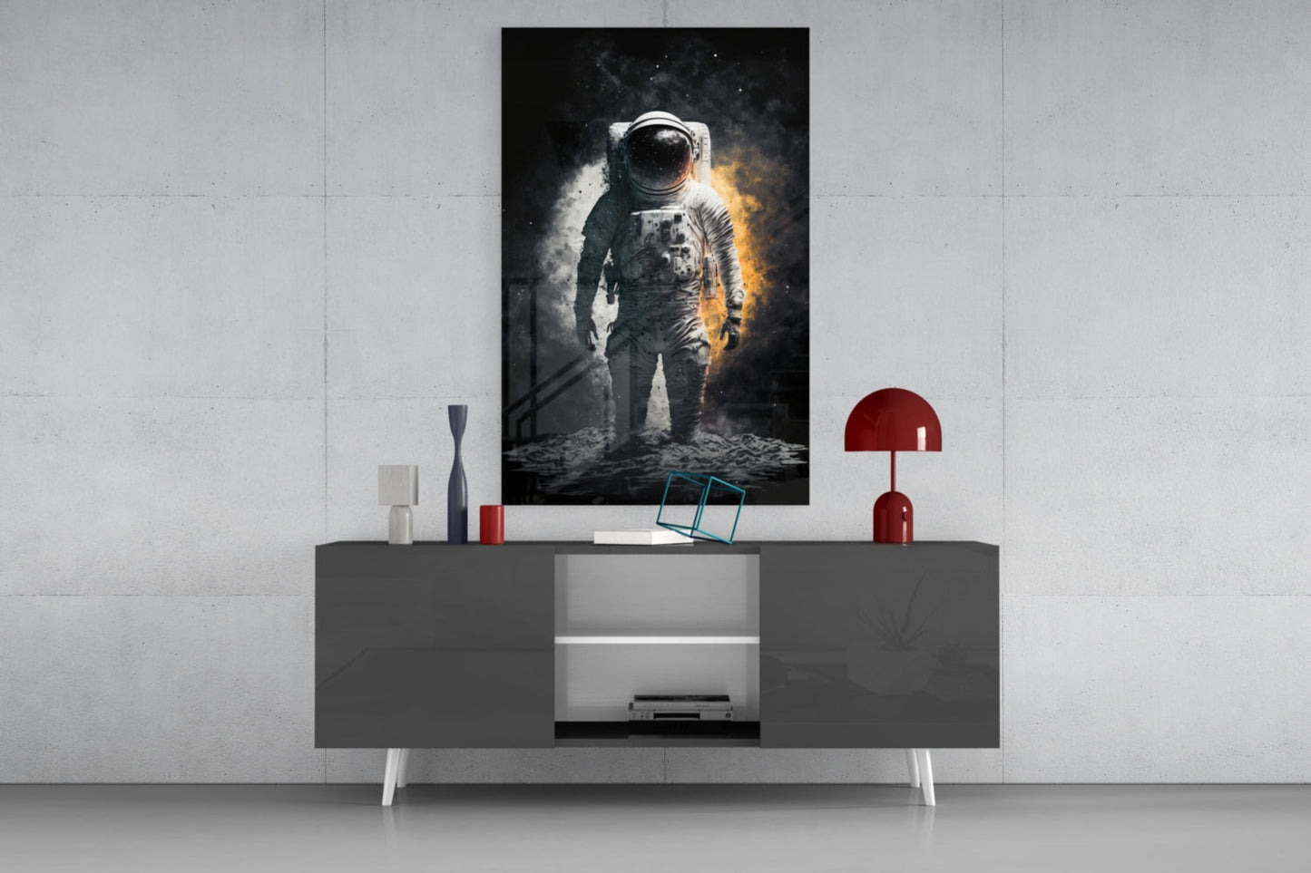 Astronaut glass wall art displayed above a gray media console with red decorative lamp and accessories in modern interior setting.