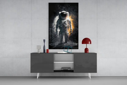 Astronaut glass wall art displayed above a gray media console with red decorative lamp and accessories in modern interior setting.