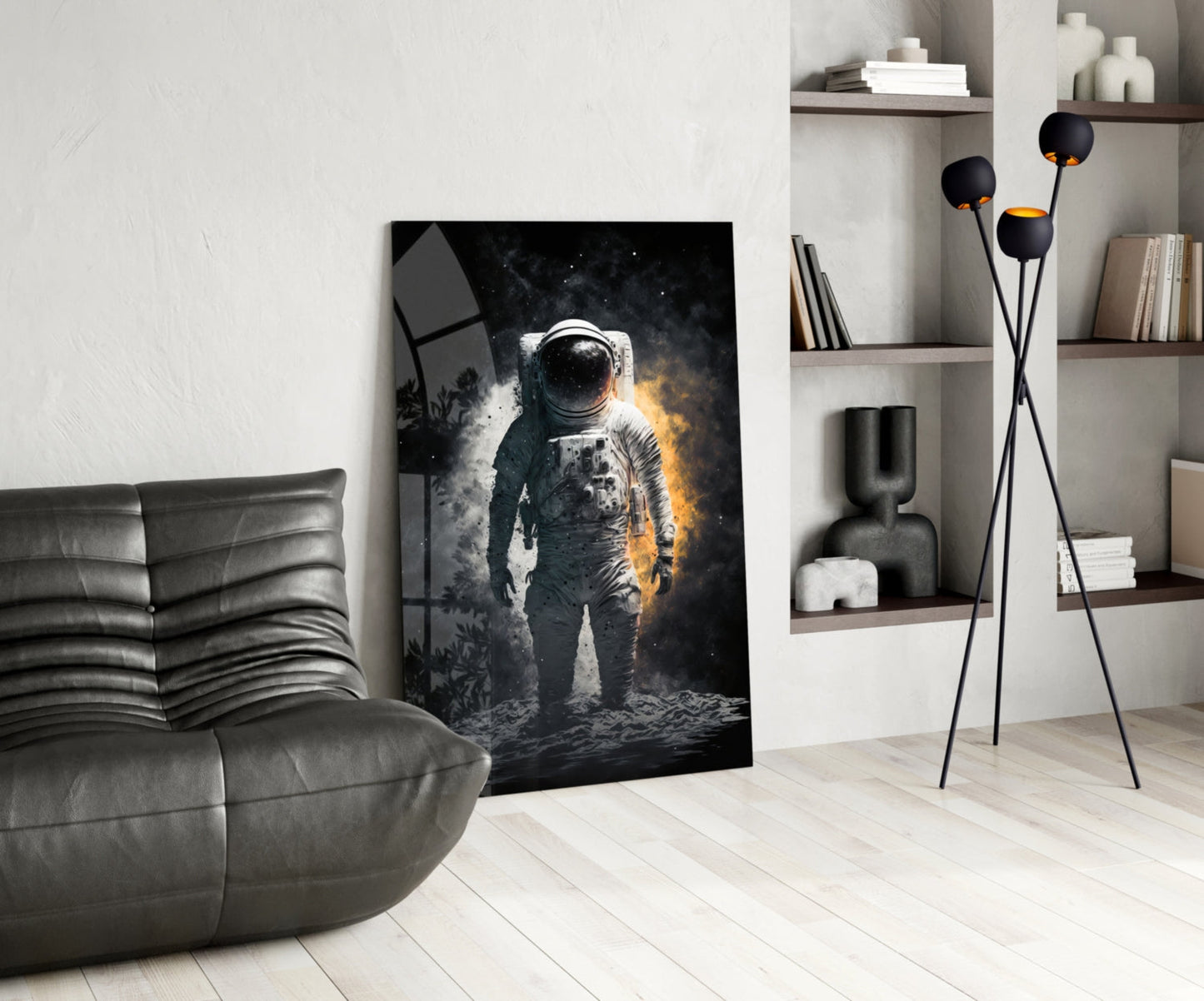 Modern living room with astronaut glass wall art leaning against white wall beside gray leather chair and black floor lamp with gold-accented spheres.