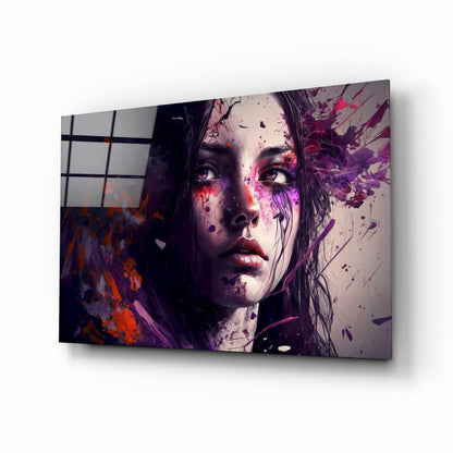 Glass wall art panel displaying a woman's face with purple and red ink splatter effects, mounted at an angle against white background.