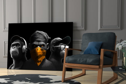 Three stylized black and white chimpanzees with gold accents displayed as glass wall art in a modern living room setting with wooden chair and paneled walls.