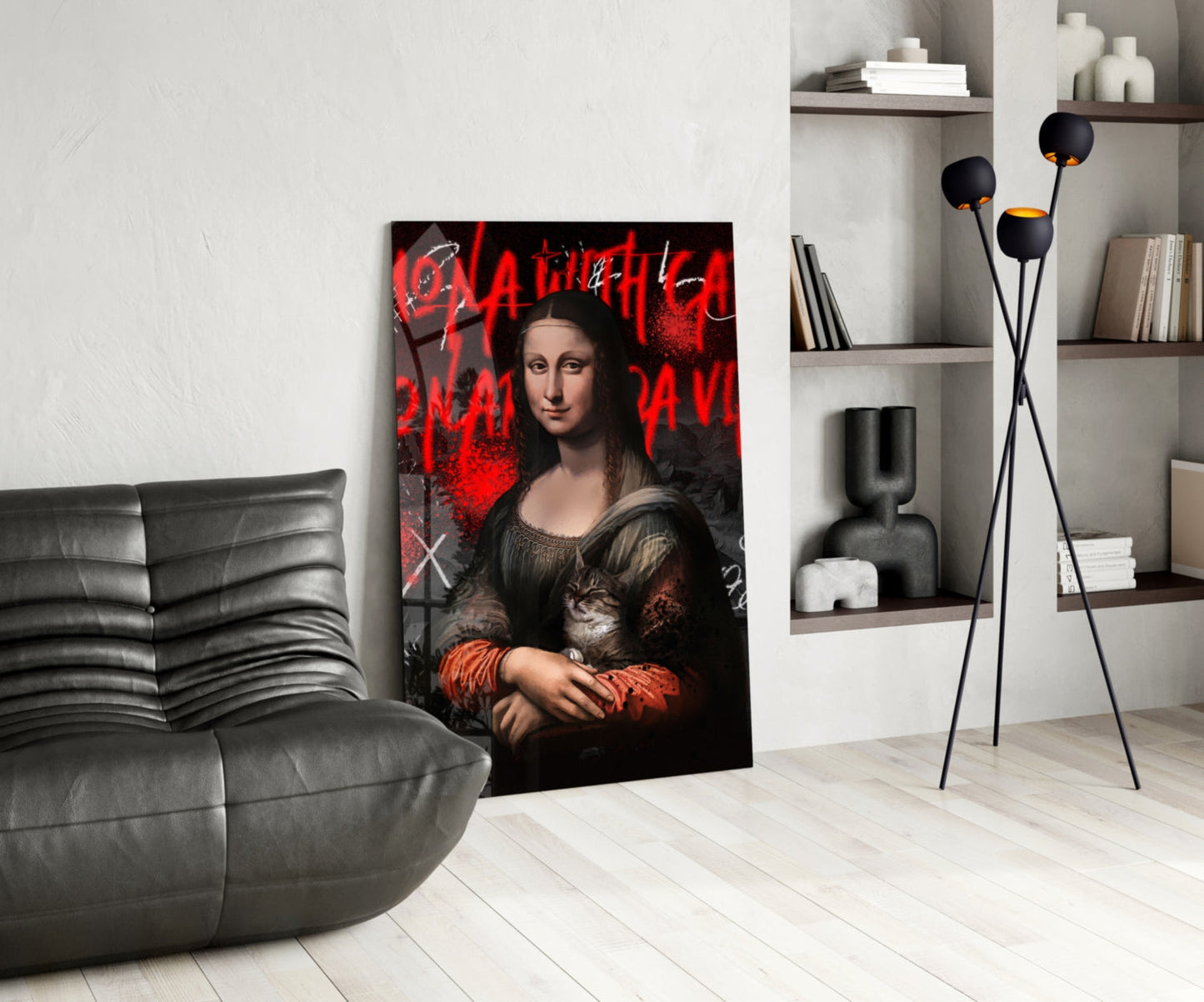Modern living room displaying glass wall art of Mona Lisa with red graffiti text and holding a cat, leaned against white wall beside gray leather chair.