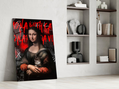 Modern interior room displaying modern art glass panel leaning against wall, featuring Mona Lisa portrait with red graffiti text overlay and cat, alongside minimalist shelving with books and décor.