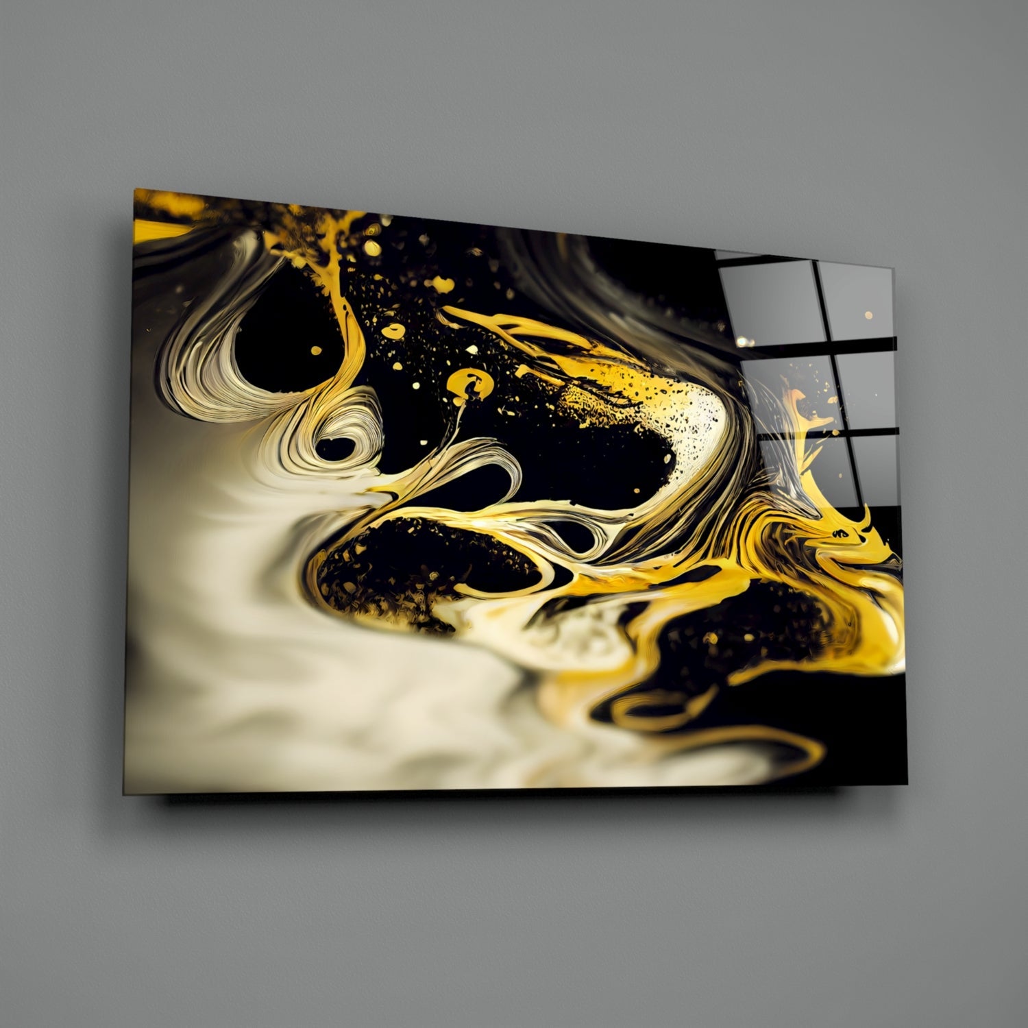 Gold and cream liquid swirls with black splashes on glass wall art mounted at an angle against gray wall.