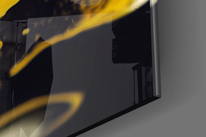 Close-up angled view of golden splash glass wall art showing bright yellow curved brushstrokes against dark background with grey wall.