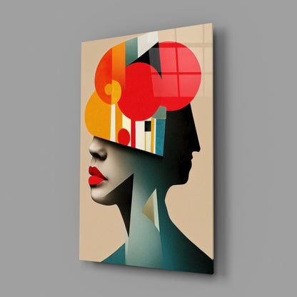 Glass wall art featuring an abstract profile of a woman's head with geometric shapes in red, orange, yellow, teal, and black on a beige background, displayed at an angle.