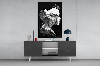 Black and white double-exposure glass wall art depicting a woman's profile silhouette filled with mountain and forest landscape, displayed above a dark console table.