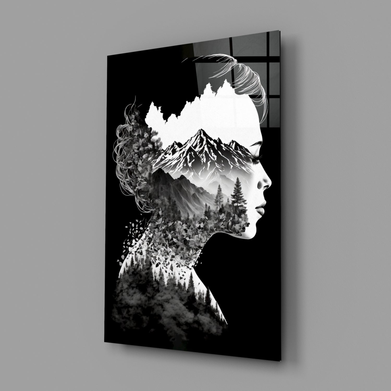 Black and white double exposure glass wall art showing a woman's profile with mountains and forest landscape integrated into her silhouette, displayed at an angle against gray background.