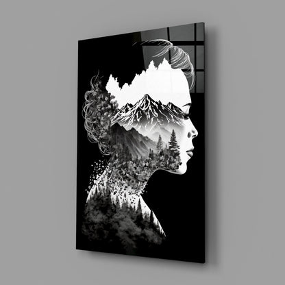Black and white double exposure glass wall art showing a woman's profile with mountains and forest landscape integrated into her silhouette, displayed at an angle against gray background.