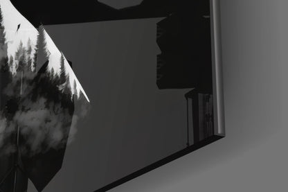 Black and white glass wall art featuring silhouetted evergreen trees with white-tipped branches displayed on interior wall.
