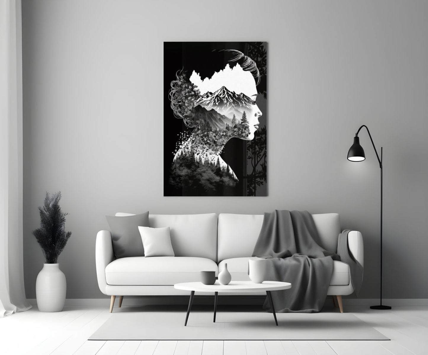 Black and white double-exposure glass art showing a woman's silhouette filled with a mountain landscape, displayed above a white sofa in a minimalist living room.
