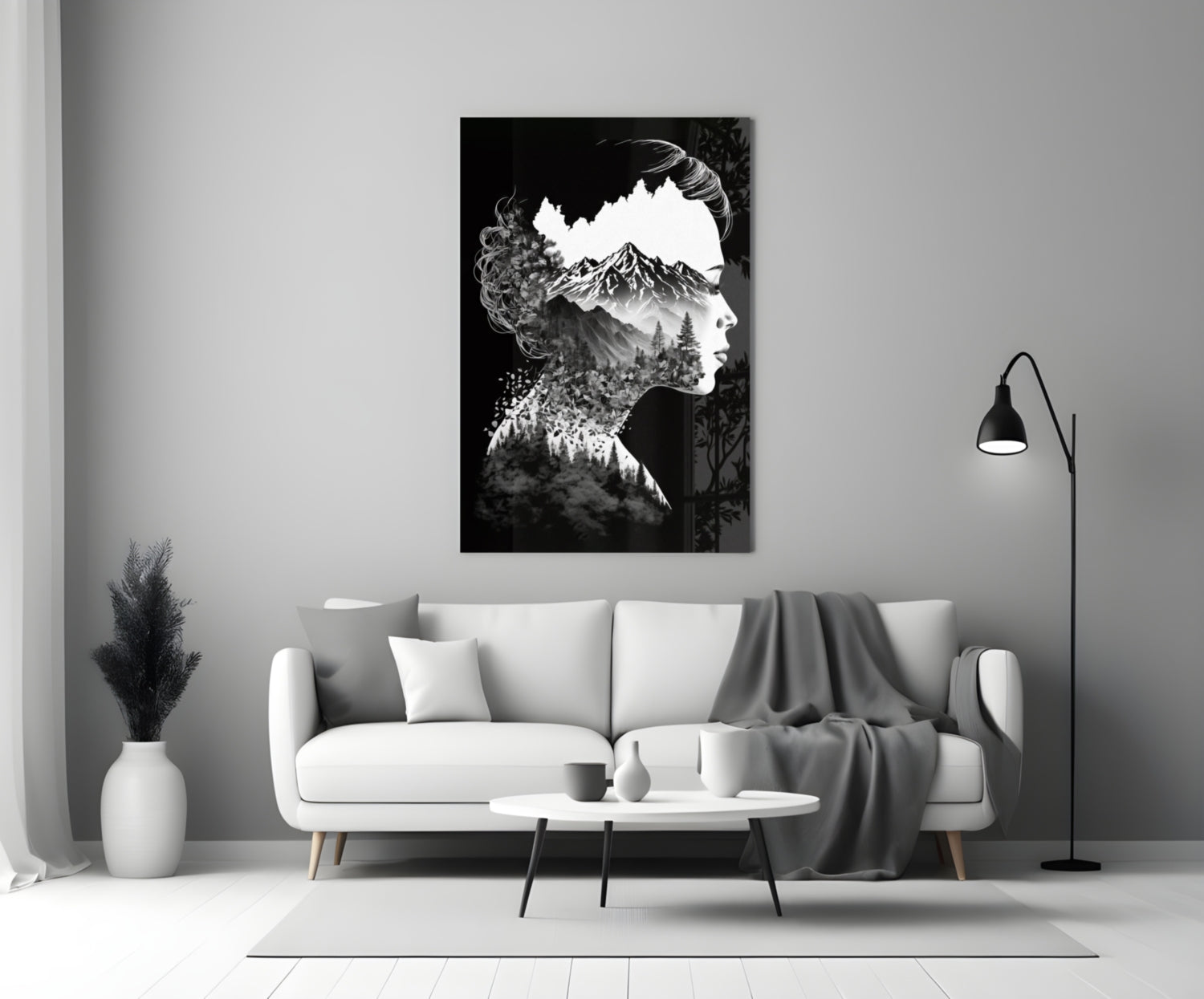 Black and white double-exposure glass art showing a woman's silhouette filled with a mountain landscape, displayed above a white sofa in a minimalist living room.